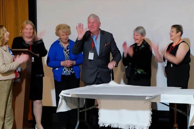 Gerry Savage, Chairperson of the Mountmellick Development association, sews the
second stitch in the bicentennial memorial piece of Mountmellick embroidery, watched by board members Frances Connelly, Eliz Moore, Mary Ging, Noreen Savage and Janet Stewart, in November
2025.
